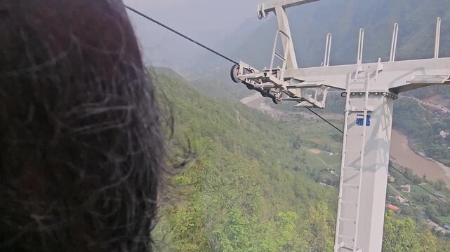 Scenic footage from the Manakamana cable car showing a passenger gondola traveling above densely forested mountain slopes, winding river valley, roads, settlements, and surrounding Himalayan foothills