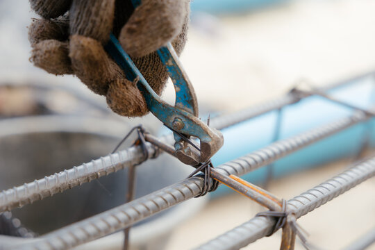 A close-up image of construction workers tying reinforcing steel bars with wire using hand-crank reinforcing steel pliers before pouring concrete.