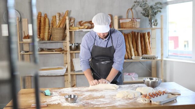 Guy works as baker in bakery, molds sausages from dough, rolls long round strips from dough. Working moment, process of creating croissants in bakery