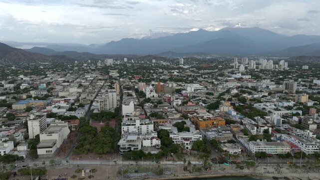Spectacular drone video of Santa Marta&rsquo;s vibrant cityscape, seaside promenade, and scenic backdrop of Sierra Nevada mountains under dramatic skies, capturing urban coastal life in soft daylight.