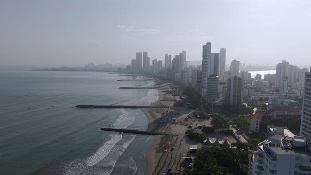 Stunning aerial footage shows Cartagena's Bocagrande coastline, with soaring skyscrapers, sunlit sandy beaches, gentle ocean waves, and tropical cityscape under soft morning light.