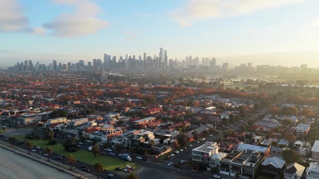 Aerial view of the Melbourne skyline at sunrise, featuring residential neighborhoods, autumn foliage, and Albert Park in the morning light in Victoria, Australia.