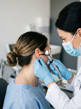 Asian Female doctor examining patient ear with otoscope in clinic office