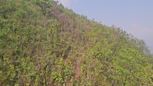 Scenic footage from the Manakamana cable car showing a passenger gondola traveling above densely forested mountain slopes, winding river valley, roads, settlements, and surrounding Himalayan foothills