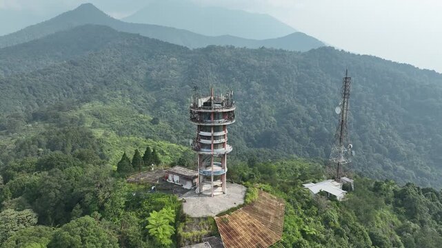 Aerial view of Puncak Pass Bogor communication tower surrounded by dense forest and lush green mountains in Kecamatan Cisarua, Jawa Barat, Indonesia.