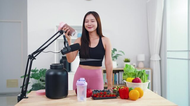Young female vlogger making diet coaching video with fruits and blender in kitchen. Asian sporty woman streaming live tutorial about organic meals and holistic wellbeing.