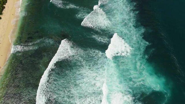 Aerial view of turquoise ocean waves crashing onto the sandy shore of Nyang Nyang Beach in Kecamatan Kuta Selatan, Bali, Indonesia.