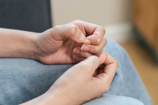 Close up of an anxious woman sitting alone and nervously picking the skin on her fingers, concept of stress, anxiety disorder, dermatillomania, and mental health struggles