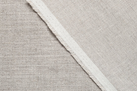 Top view of natural beige linen fabric texture with a frayed edge. Ideal for backgrounds, textile projects, rustic design, fashion and crafting materials.