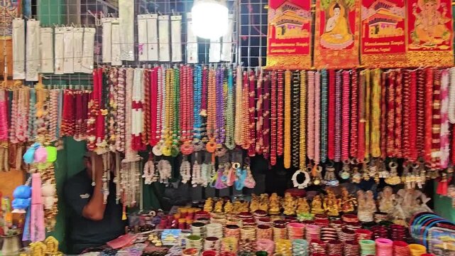 Colorful souvenir and religious items displayed at a market stall near Mankamana Temple in Nepal. The shop features prayer beads, malas, bracelets, decorative items, bells