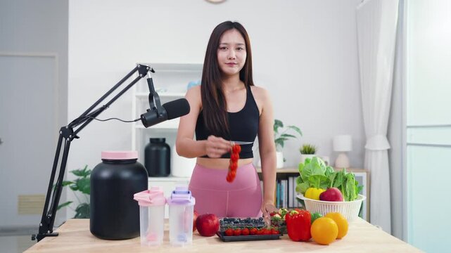 Asian fitness influencer recording healthy nutrition vlog with smartphone camera. Young female content creator talking about diet, fresh organic food and wellness lifestyle.