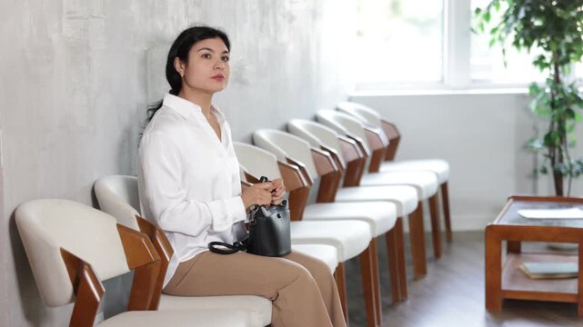 Woman sits in waiting room, awaiting appointment with specialist at clinic or travel agency.