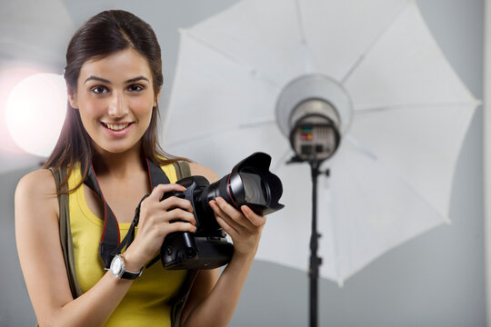 Portrait of young female photographer with digital camera in studio 