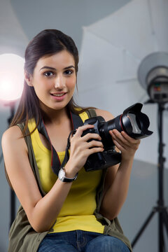 Portrait of young female photographer with camera sitting in studio 