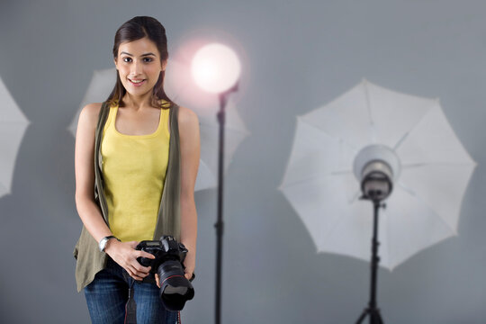 Portrait of young female photographer with camera standing in front of spotlight in studio 