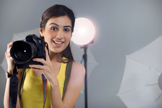 Portrait of young female photographer with digital camera in studio 