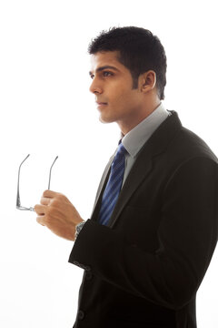 Thoughtful businessman holding glasses over white background 