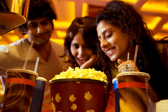 Happy friends looking at popcorn and soft drink 