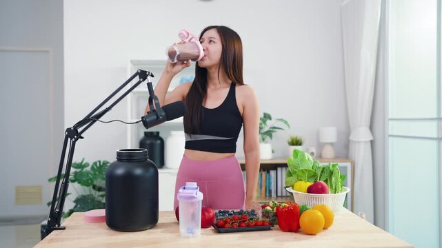 Young female vlogger making diet coaching video with fruits and blender in kitchen. Asian sporty woman streaming live tutorial about organic meals and holistic wellbeing.