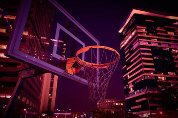 Basketball hoop on a court with city buildings at night © Cavan