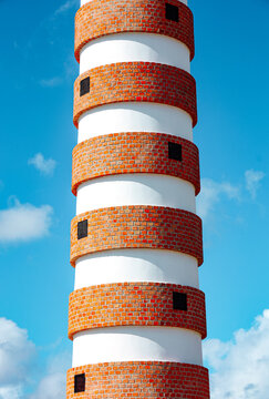 Striped red brick lighthouse tower against blue sky
