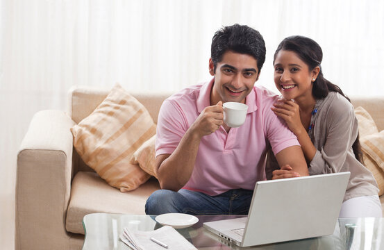 Portrait of happy young couple smiling with laptop and coffee cup 