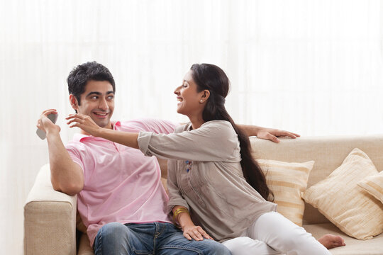 Playful young man keeping remote control away from woman 