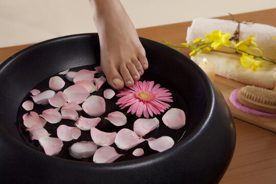 Close-up of a woman's feet and a bowl filled with water and rose petals 
