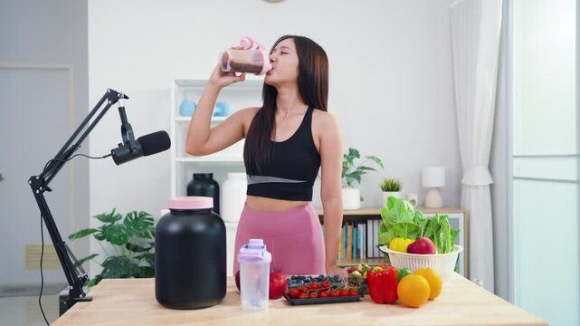 Young female vlogger making diet coaching video with fruits and blender in kitchen. Asian sporty woman streaming live tutorial about organic meals and holistic wellbeing.
