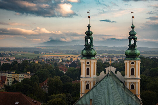 Panorama Nysy z widokiem na barokowy kości&oacute;ł pw. Świętych Apostoł&oacute;w Piotra i Pawła na pierwszym planie oraz pasmo g&oacute;rskie w tle oraz chmurami burzowymi