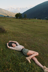 Naklejka premium Relaxed woman lies on a grassy meadow in a wide field, enjoying outdoor lifestyle under warm sun, casual pose and peaceful nature vibes in a rural landscape