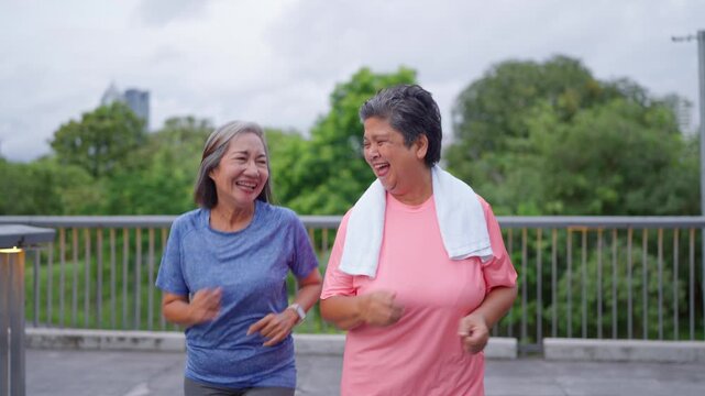 Two happy Asian senior women jogging exercise outdoors in modern city. 