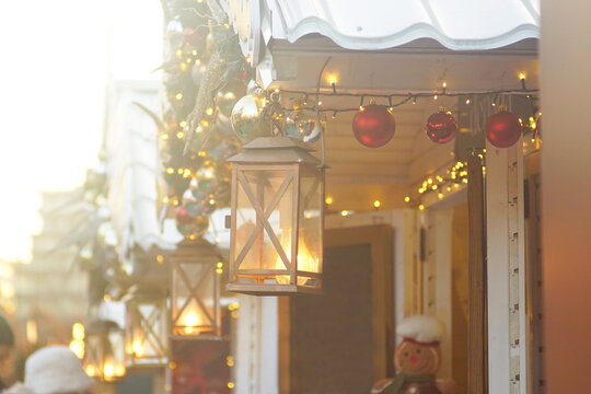 Glowing vintage lantern lighting wooden festive booth decorated with red baubles and garlands. Depicts local holiday fair culture, traditional European street shopping, and Christmas market charm.
