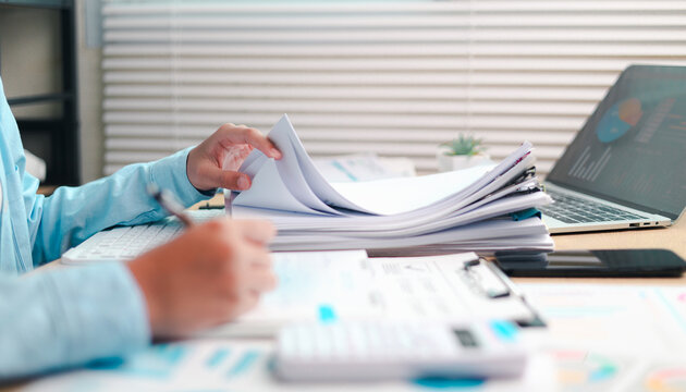 Reviewing business documents at an office desk, organizing paperwork and reports for administrative workflow, financial planning, data analysis