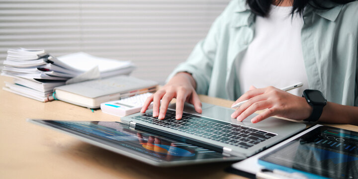 Businesswoman working on a laptop with tablet, smartphone, calculator, and documents, data analysis, financial planning, and workflow.