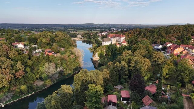 Aerial view of Ozalj Castle and Kupa River surrounded by lush forests and residential houses in Ozalj, Karlovac County, Croatia.
