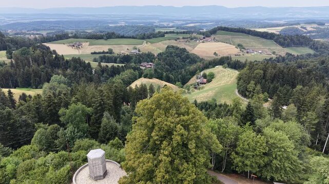 Aerial view of the rolling green hills and forests of the Emmental region with a stone monument and large trees in Emmental District, Canton of Bern, Switzerland.