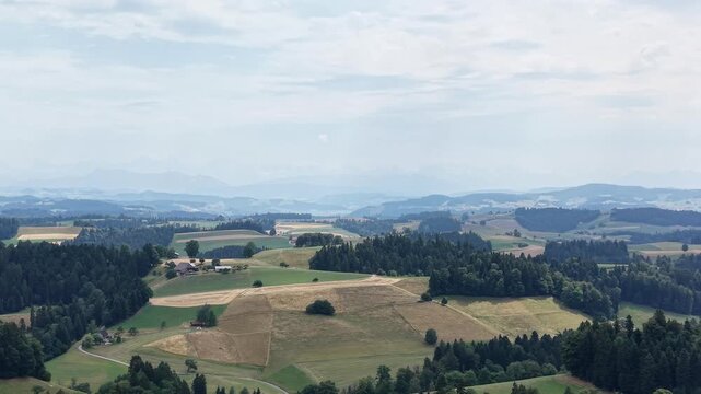 Aerial view of rolling green hills, agricultural fields, and dense forests surrounding traditional farmhouses in Emmental District, Canton of Bern, Switzerland.