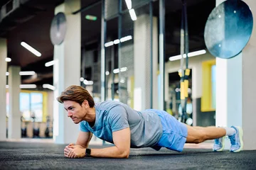 Fototapete Fitnessstudio Man doing a plank exercise on gym floor, building core strength and endurance. Fitness and healthy lifestyle concept  © we.bond.creations