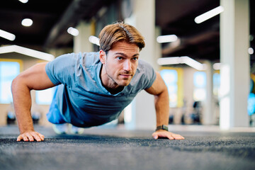 Fototapeta premium Young man performing pushup exercise on gym floor, focusing on strength, training, and a healthy lifestyle