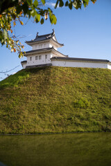 Vertical view of a Japanese castle turret and walls with tree leaves and pond reflection © KotoriFlower