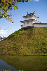 Vertical view of a Japanese castle turret and walls with tree leaves and pond reflection © KotoriFlower