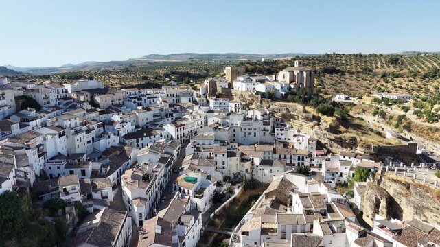 Aerial view of the white village of Setenil de las Bodegas with its unique houses built into the rock cliffs under a clear blue sky in Setenil de las Bodegas, Andalusia, Spain.