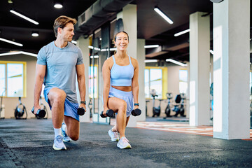 Fototapeta premium Athletic couple training together, doing lunges with dumbbells during a fitness workout for strength and healthy lifestyle