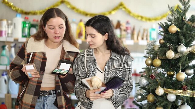 Women choose a set of cosmetics and hair combs against the background of the Christmas tree. Customers in a New Year's supermarket shop for cosmetics and accessories . High quality 4k footage
