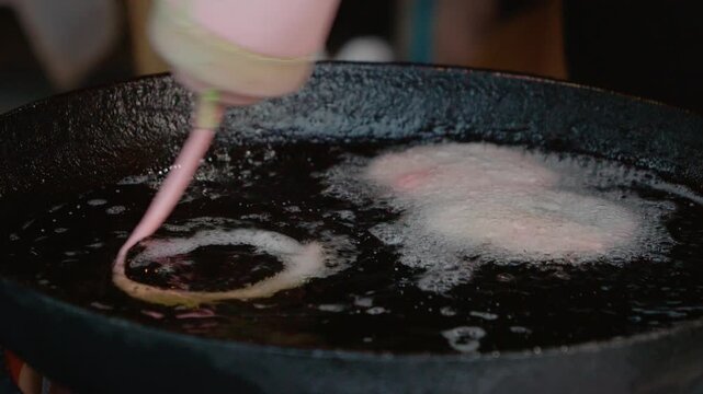 Jalebi is being prepared in hot oil on the street during a local festival. The bright colors and sweet aroma attract many people nearby.