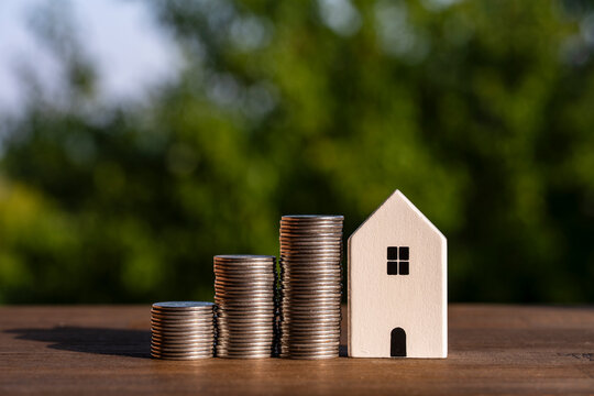 Investment in real estate concept. Wooden model house with increasing stacks of coins on table, symbolizing property growth, savings, mortgage, home finance, or buying new house