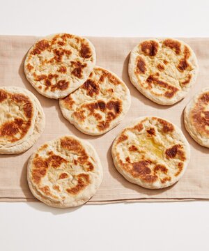 Vegetarian flatbreads with blistered crusts arranged on a textured linen cloth, featuring a golden oil sheen for menu and packaging designs