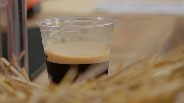 A glass of dark beer is set on a table during a street food festival. After a moment, it is picked up and taken away. People enjoy food and drinks in the background.