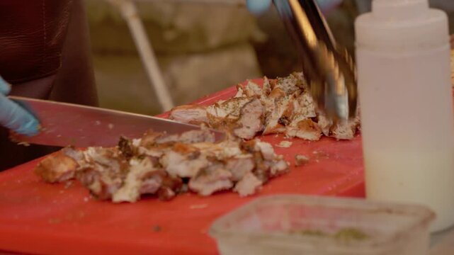 Cook slices grilled meat on a chopping board during a busy street food festival. Vendors prepare and serve food to festival-goers enjoying the atmosphere.